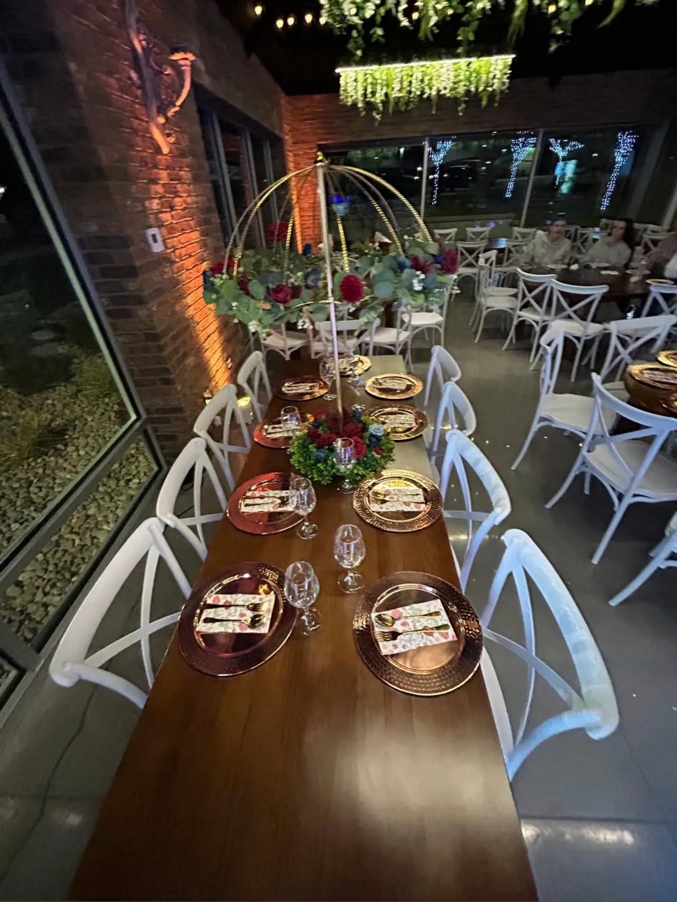 A long table with copper chargers under a gold dome of red flowers