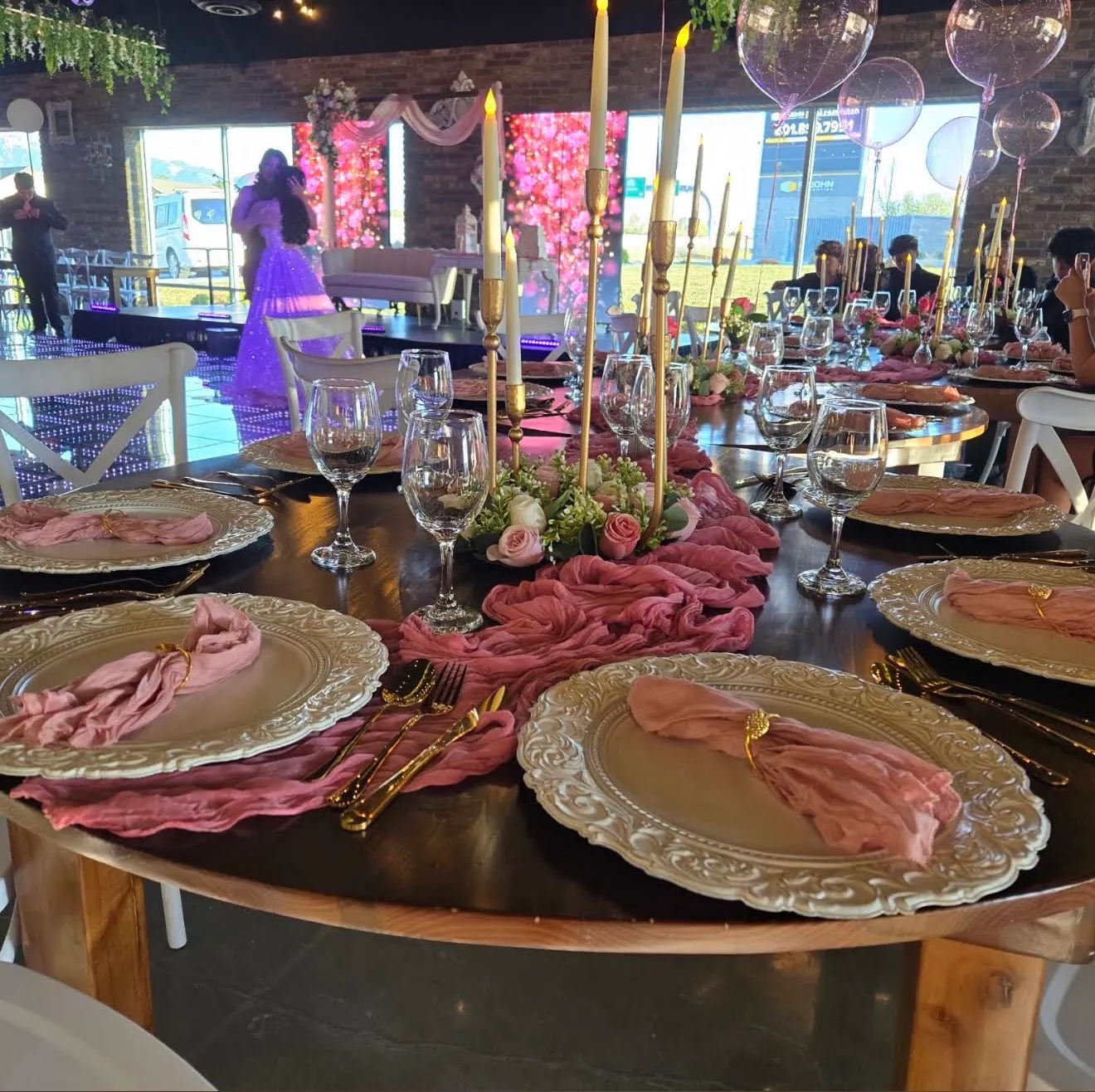 A table with carved chargers, pink napkins and gold candelabras; the waltz on the floor behind