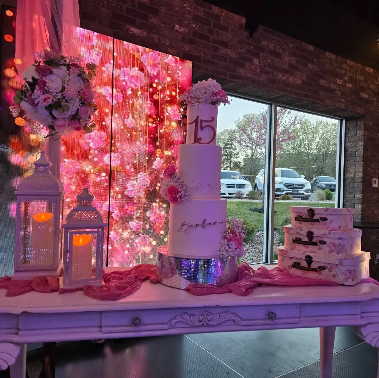A quinceañera cake with pink flowers in front of a floral LED screen