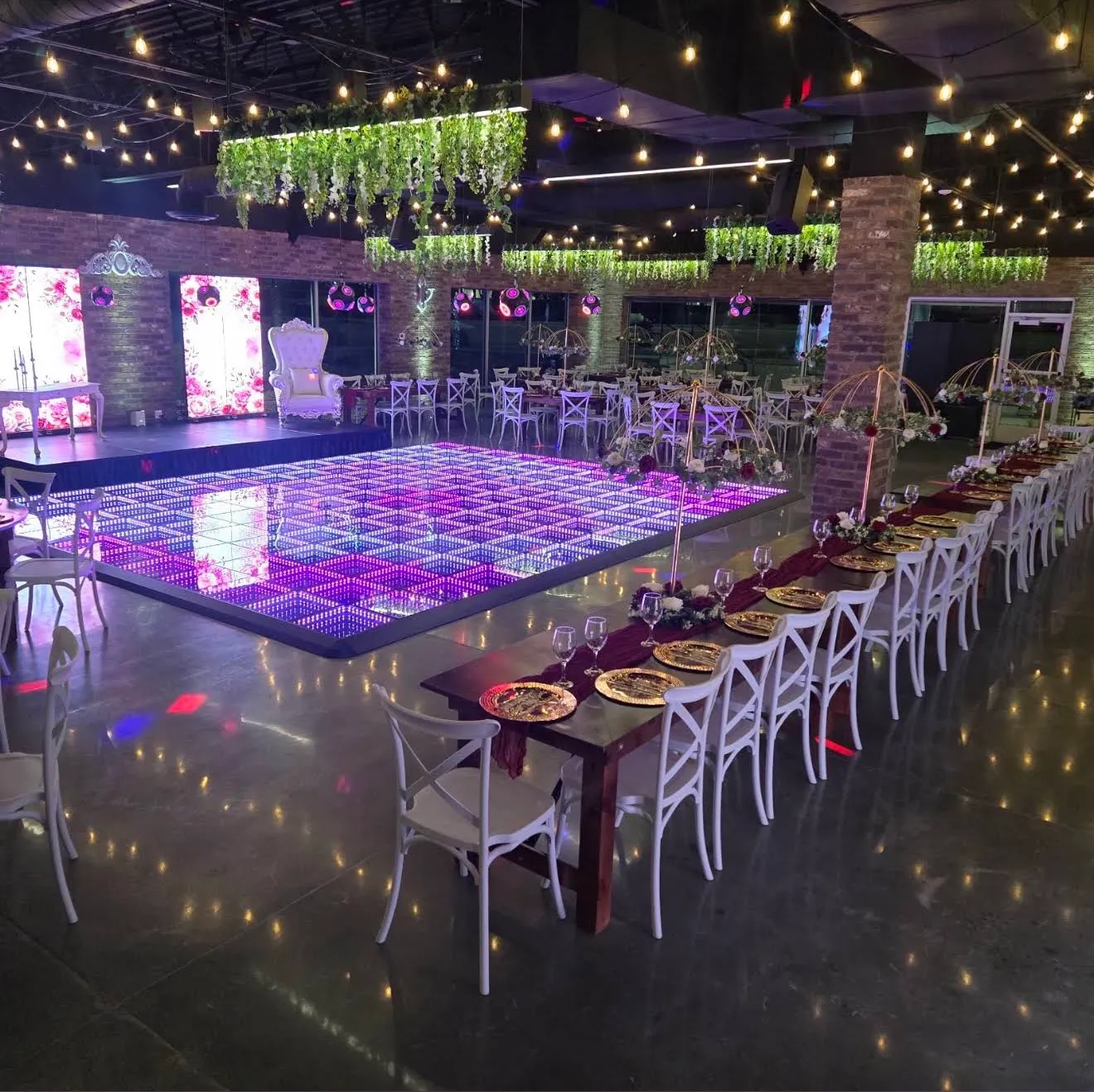 The room at night: lit LED dance floor, white throne, long tables and string lights